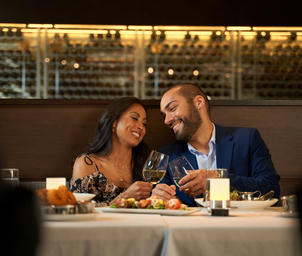 A smiling couple sitting in a restaurant booth eating dinner and drinking wine